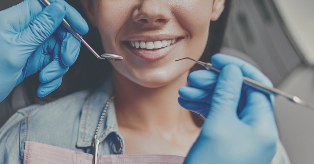 Dental patient smiling. The smile is framed by dental instruments being held by a dentist