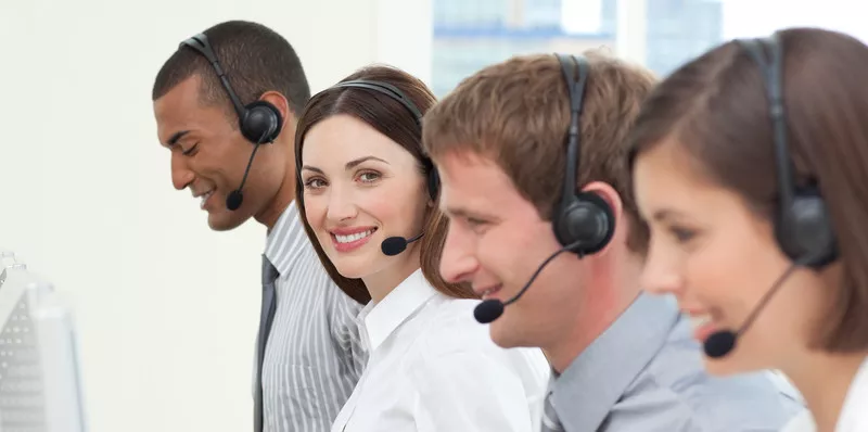 Four people wearing headsets and working at computers. One worker is facing the camera and smiling.